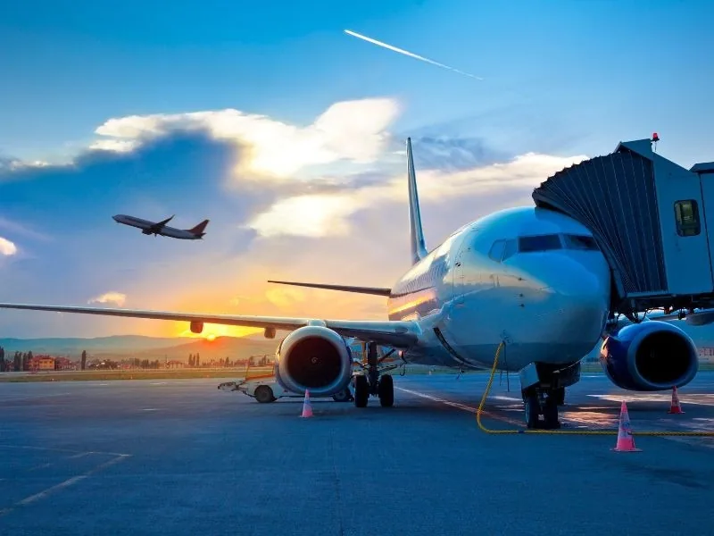Avião estacionado no pátio enquanto outro decola ao fundo