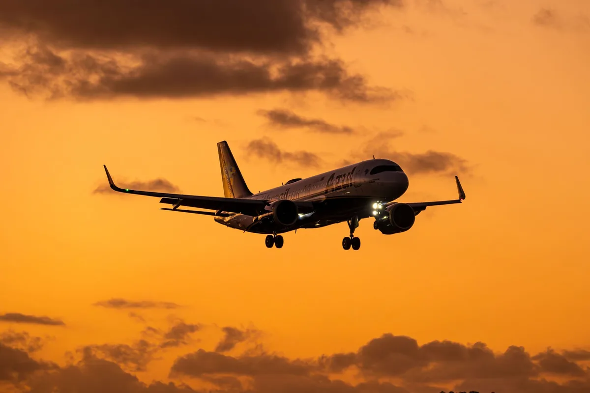 Avião comercial em aproximação final para pouso, com o céu alaranjado do entardecer