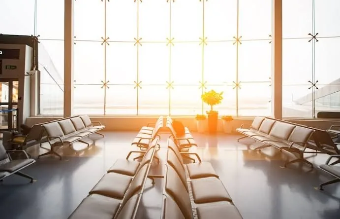 Saguão de embarque vazio, com poltronas e luz da manhã entrando pela vidraça
