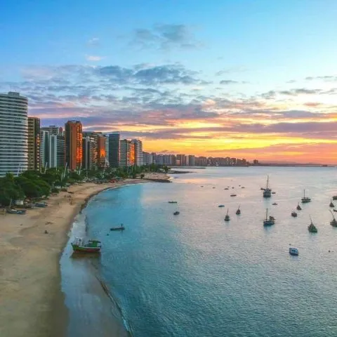 Orla de Fortaleza ao entardecer, com os prédios da Beira-Mar e barcos na água