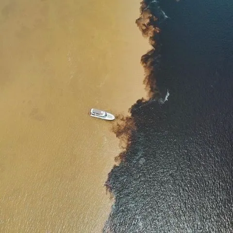 Barco em rio amazônico visto de cima, com as duas cores da água