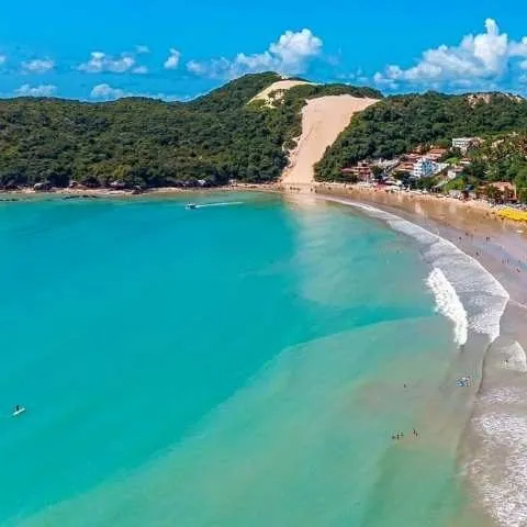 Praia com barcos ancorados e falésia ao fundo, no litoral potiguar
