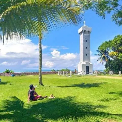 Gramado com farol branco e uma pessoa sentada à sombra