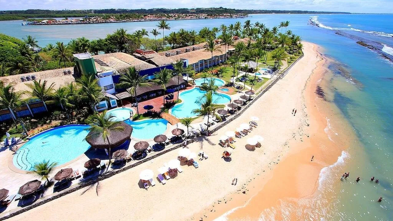 Resort à beira-mar com piscina, coqueiros e a praia ao fundo